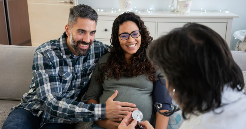 Expecting mother and father at home during a prenatal visit while mom has blood pressure taken by a midwife