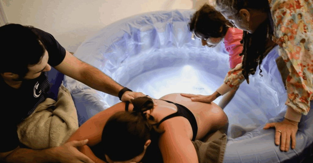 A man providing help to his partner during labor while midwives also help