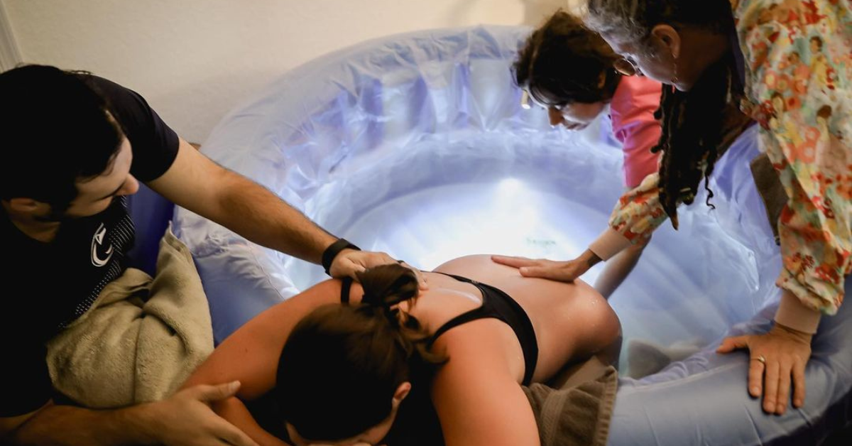 A man providing help to his partner during labor while midwives also help